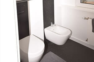 Weißes WC und Bidet in hellem Badezimmer mit dunklem Boden